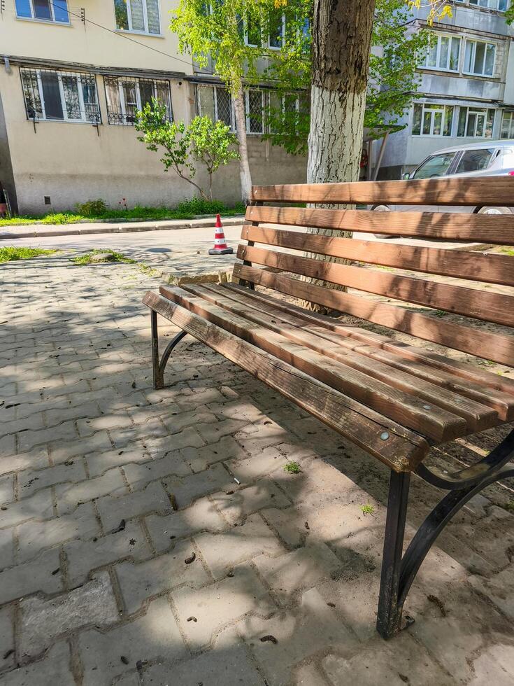 A wooden bench is sitting on a brick sidewalk in front of a building. The bench is empty and the sun is shining on it photo