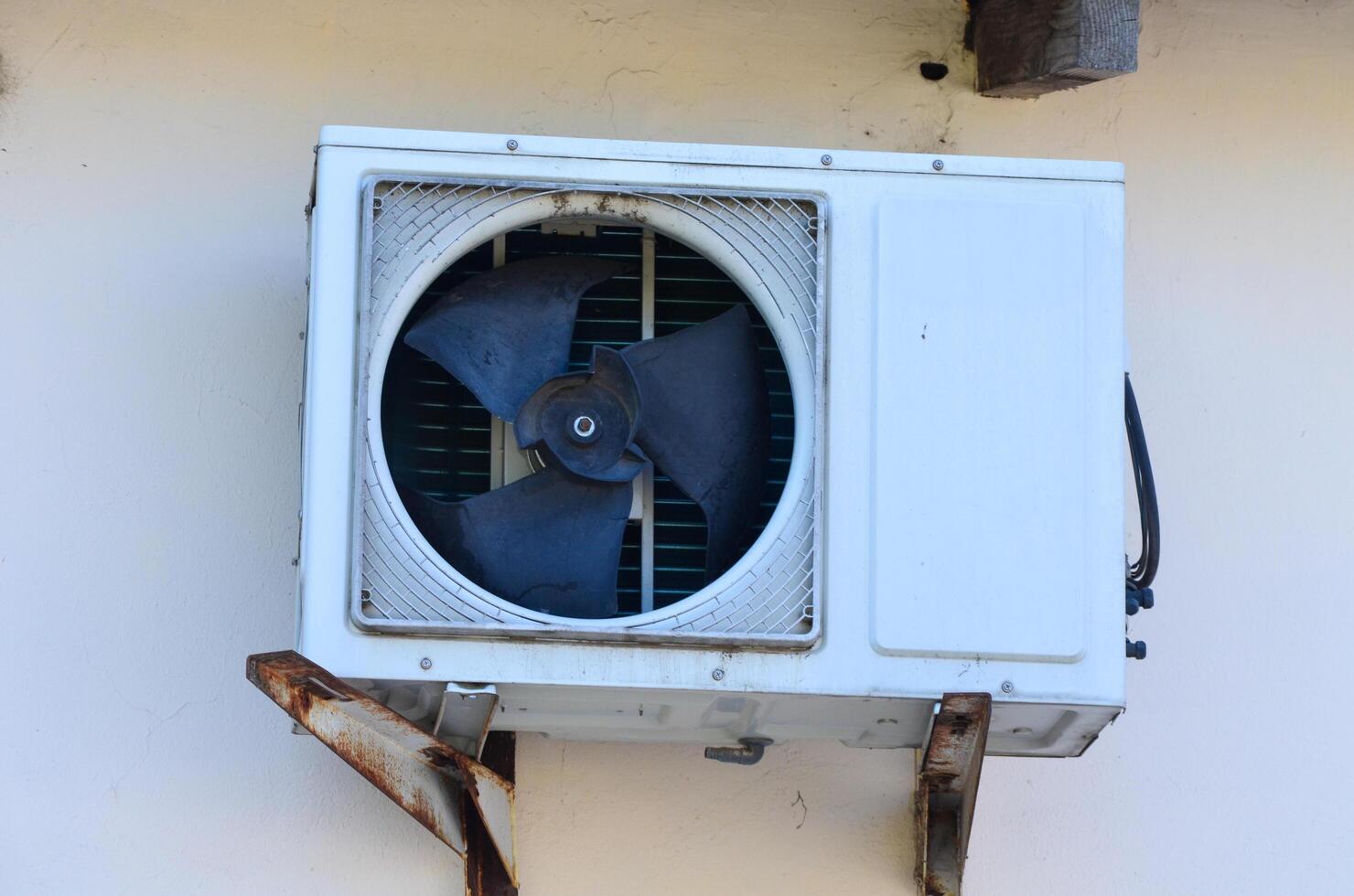 A white air conditioner with a black fan on it. The fan is broken and the air conditioner is not working photo