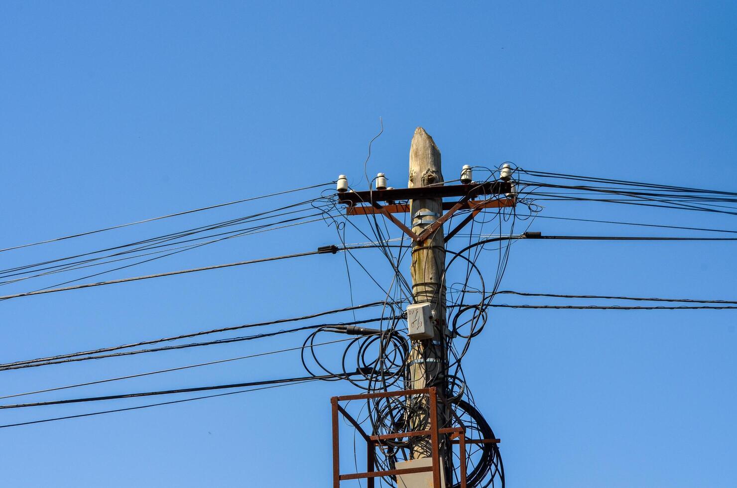 A tall pole with many wires coming out of it. The sky is blue and clear. The pole is surrounded by a metal box photo