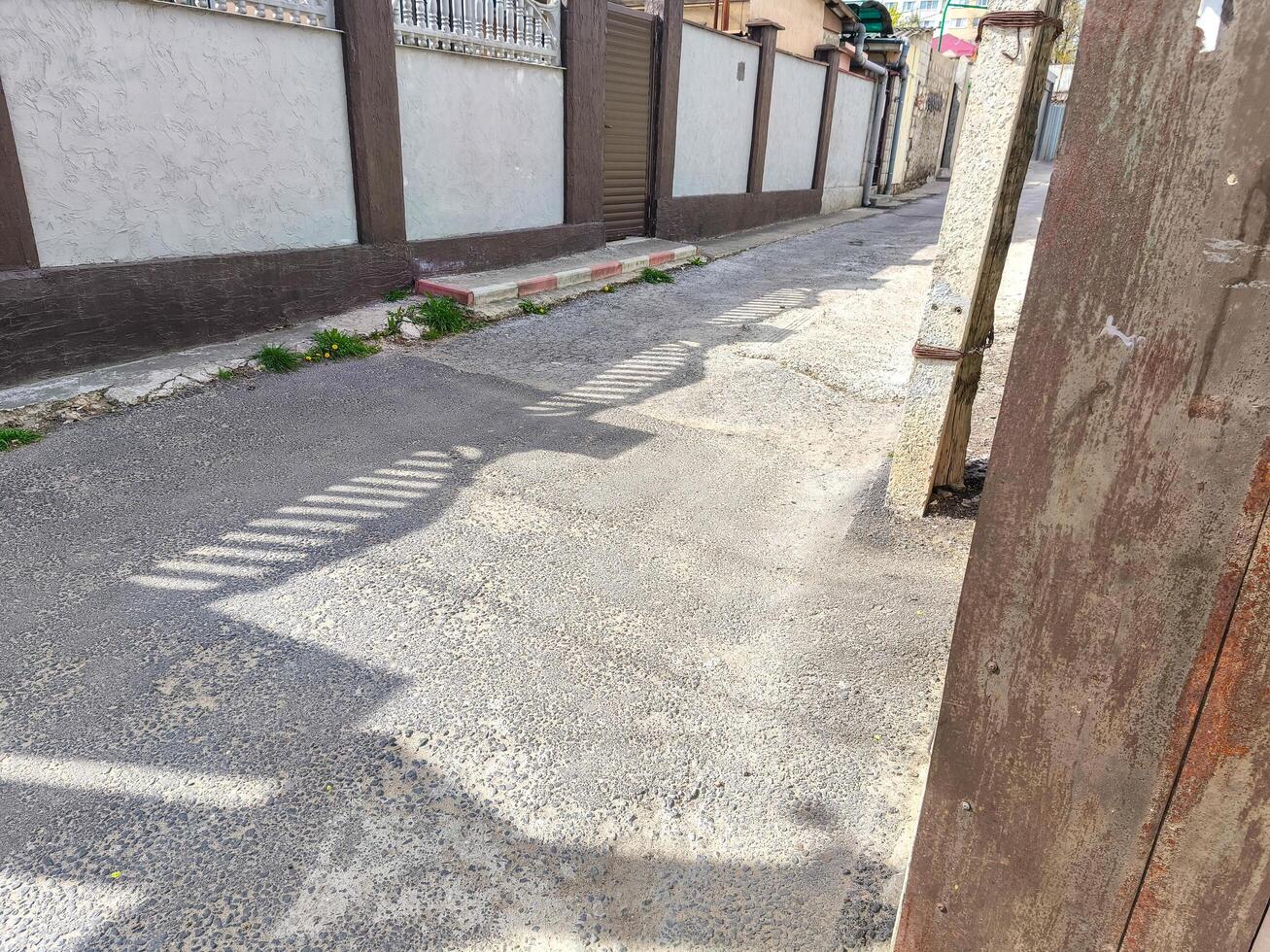 A street with a sidewalk and a fence. The sidewalk is empty and the street is empty. The fence is brown and has a green stripe photo