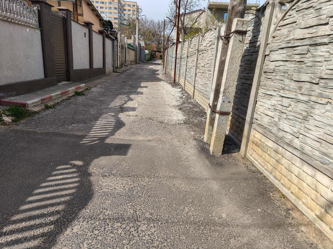 A street with a fence on the side. The fence is made of concrete and has a few holes in photo
