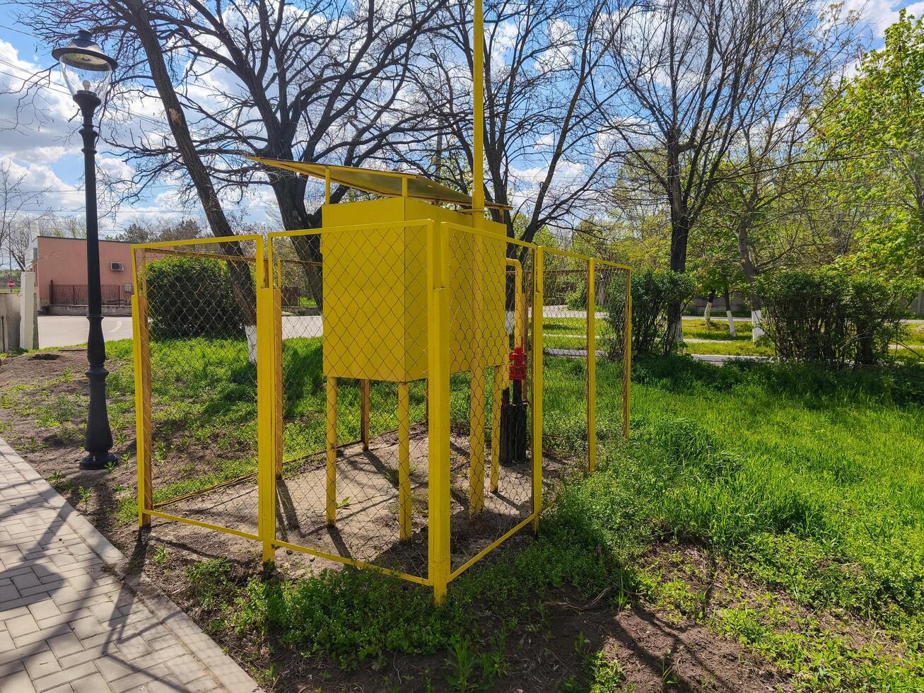 A yellow box with a red fire hydrant on top of it. The box is surrounded by a fence photo
