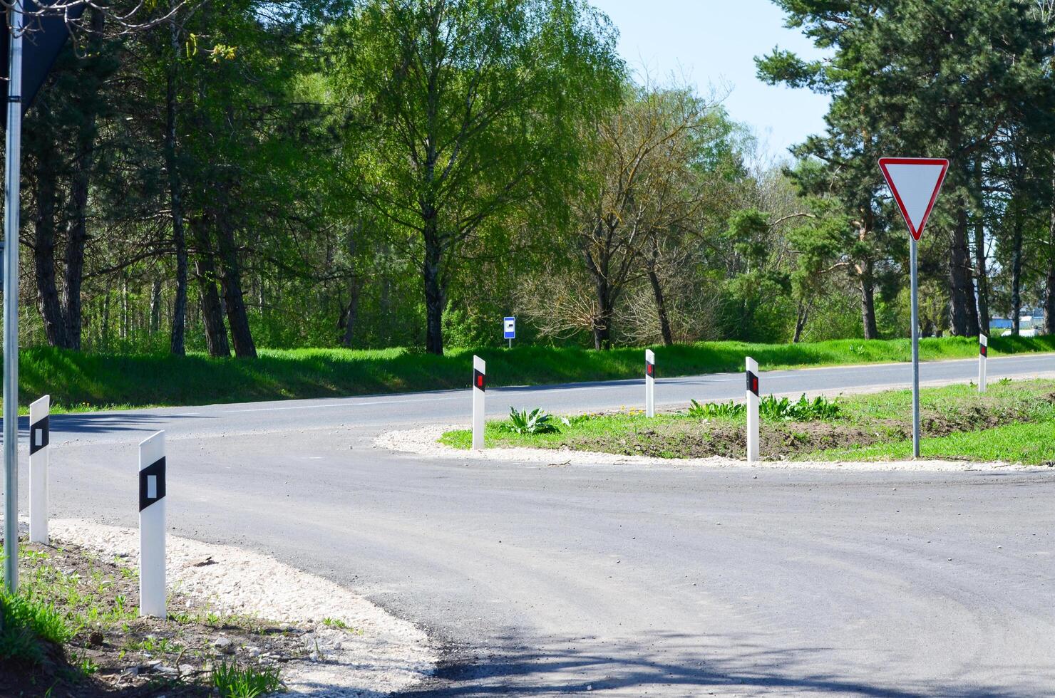 A road with a white line and a red and white sign. The road is curvy and has a lot of trees in the background photo