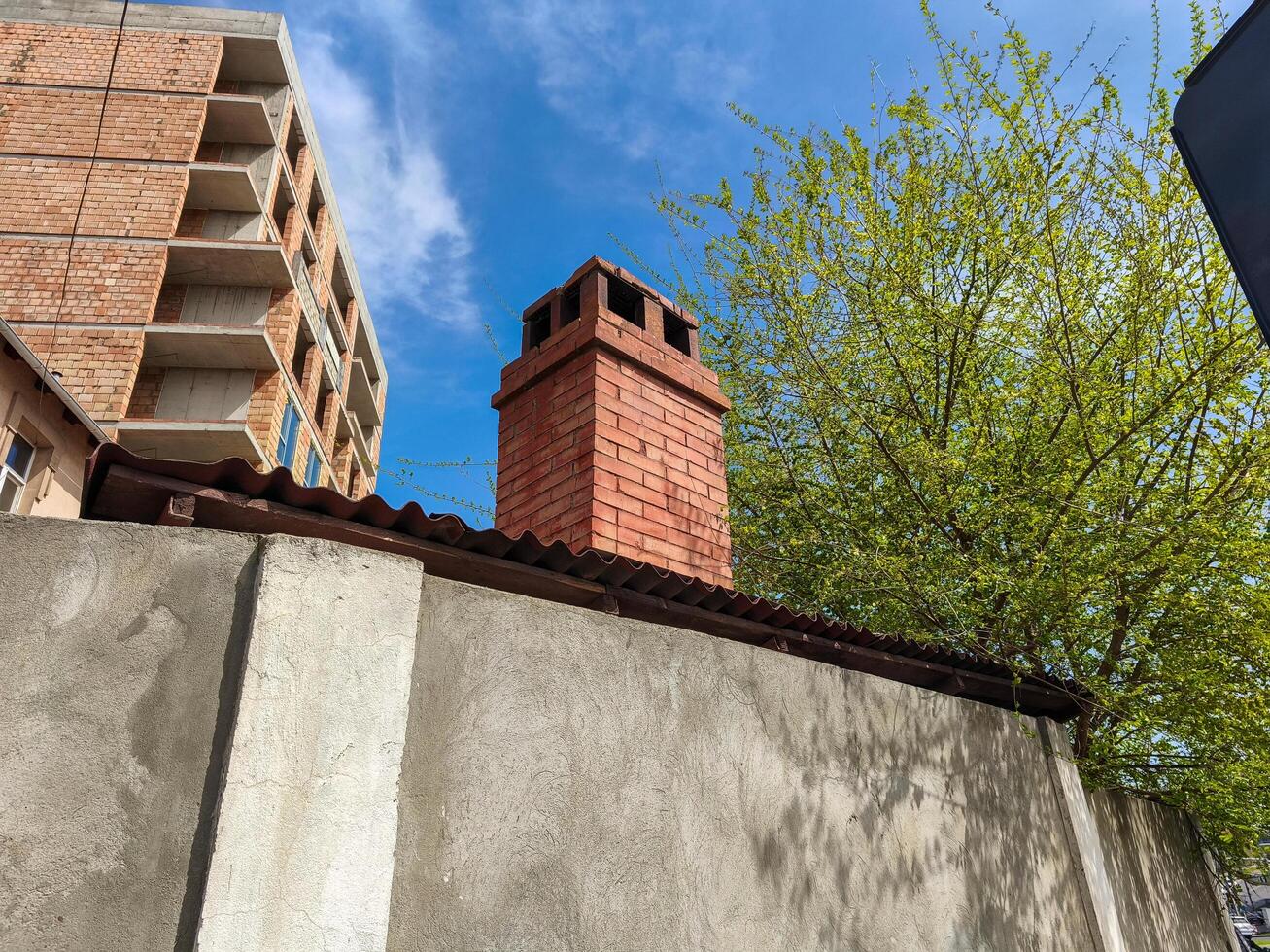 A brick building with a chimney on top. The chimney is red and has a metal roof. The sky is blue and there are no clouds photo