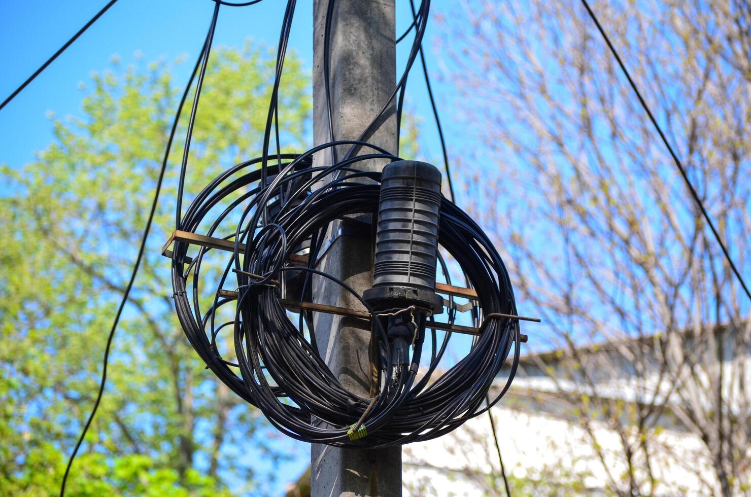 A black wire is wrapped around a pole. The wire is tangled and twisted. The sky is blue and clear photo
