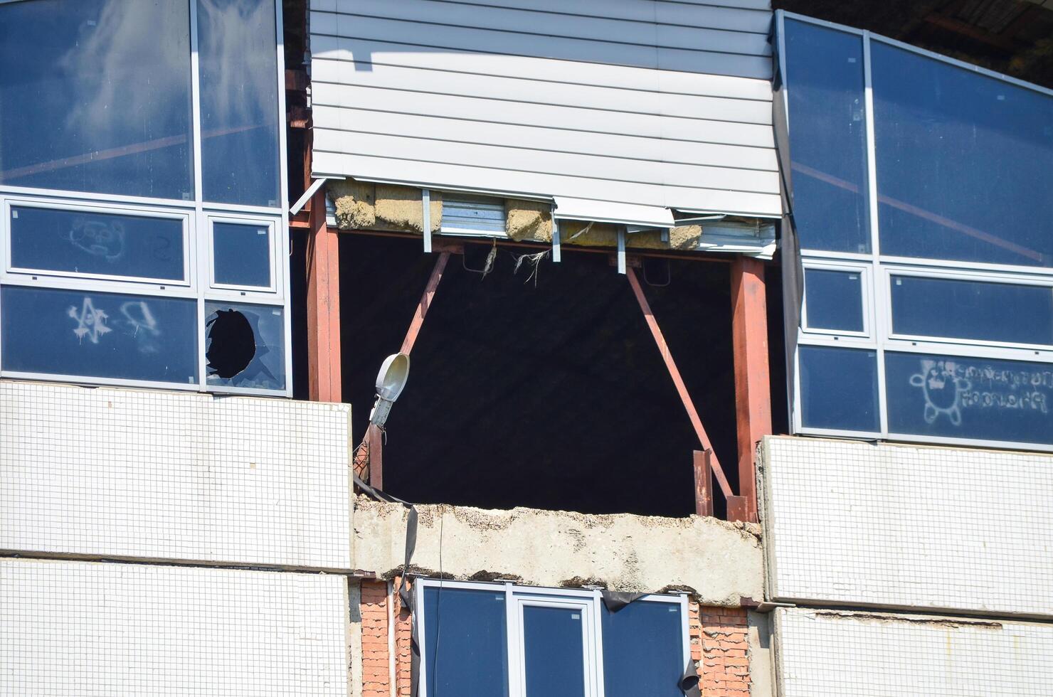 A building with a hole in the wall and a window with graffiti on it. The building appears to be in disrepair photo