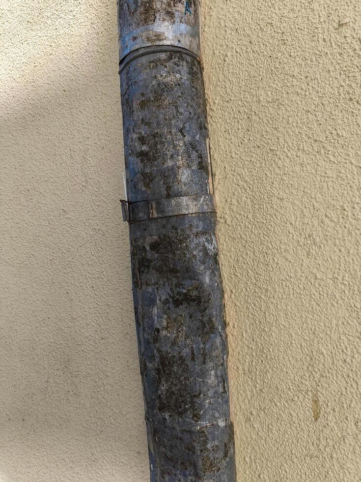 A rusty pipe is leaning against a wall. The pipe is covered in dirt and has a few holes in it photo