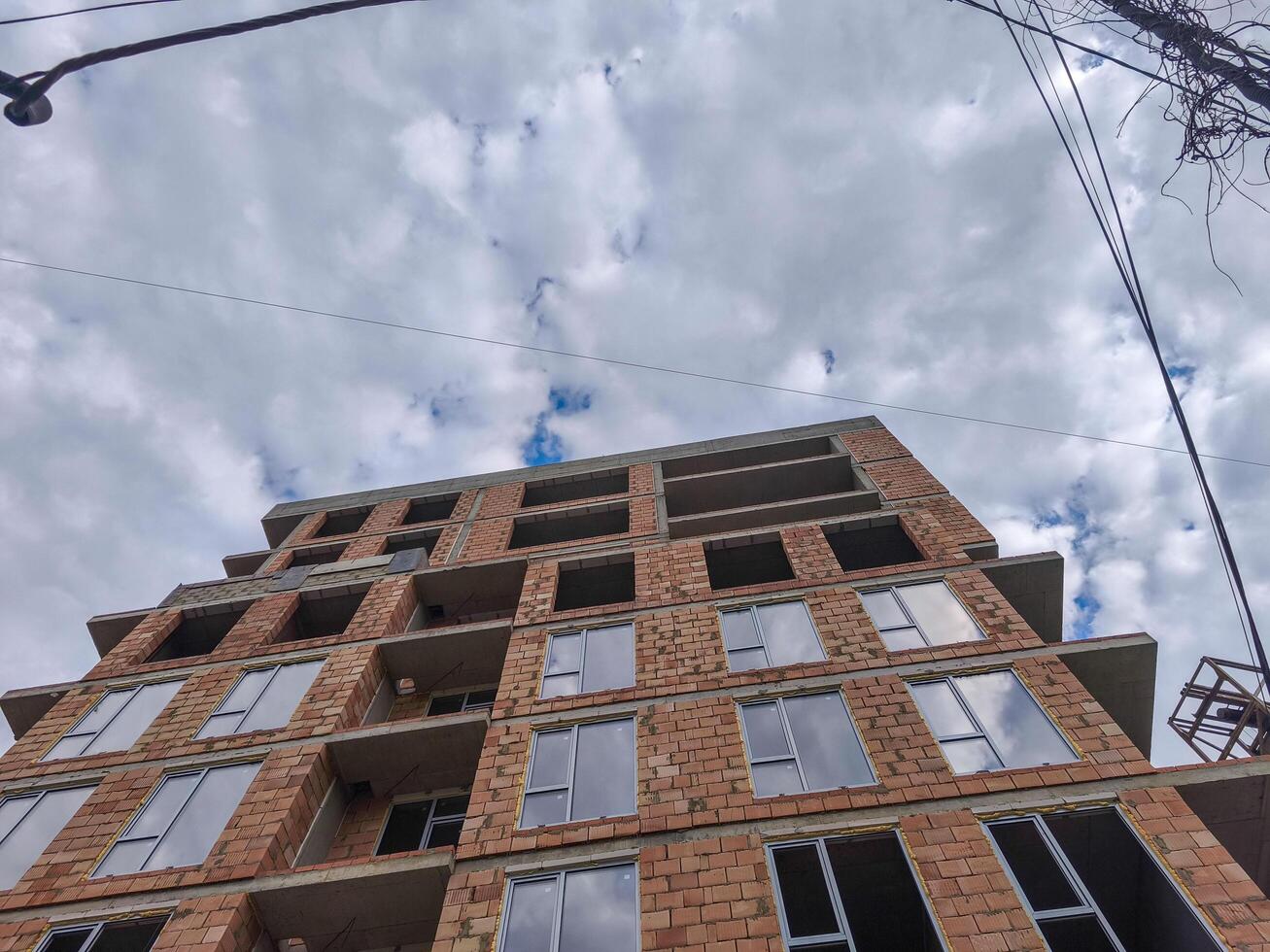 A large brick building with a cloudy sky in the background. The building is under construction and has a lot of windows photo