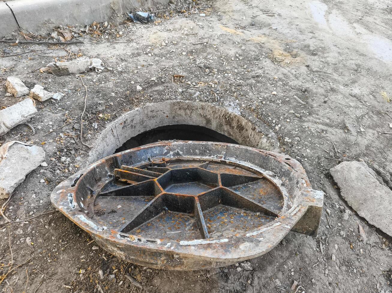 A rusty metal object is sitting in a hole in the ground. The object is likely a drain cover or a pipe. The scene is somewhat eerie and abandoned, with the object sitting alone in the dirt photo
