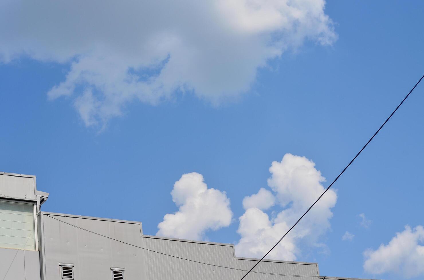 A blue sky with a few clouds and a power line. The sky is clear and bright, and the clouds are scattered throughout the sky. The power line is visible in the background photo