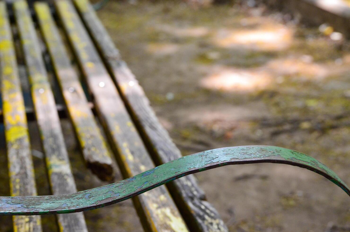 A bench with a green metal arm rests. The bench is old and has a yellow paint photo