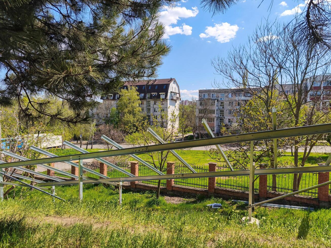A fence with a row of solar panels on it. The fence is in front of a building with a lot of windows photo