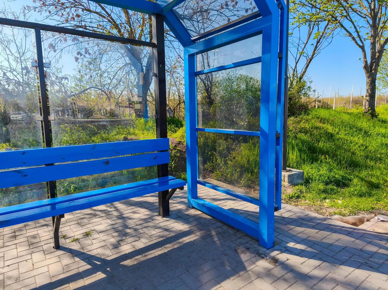 A blue bus stop with a bench and a door. The bench is empty. The sky is blue and the grass is green photo