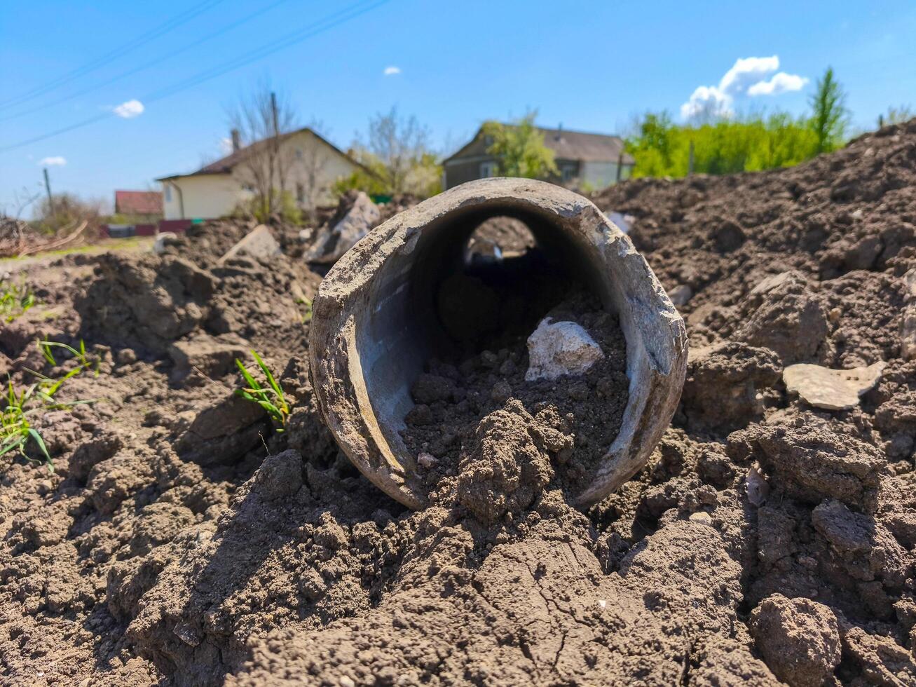 A pipe is laying on the ground in a field. The pipe is broken and has a hole in it. The ground is covered in dirt and rocks. The scene is desolate and abandoned photo