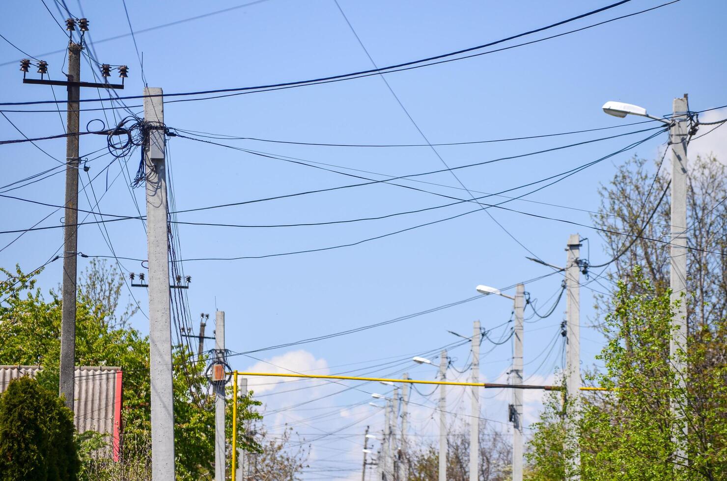 A street with many power lines and a few trees. The sky is clear and blue photo
