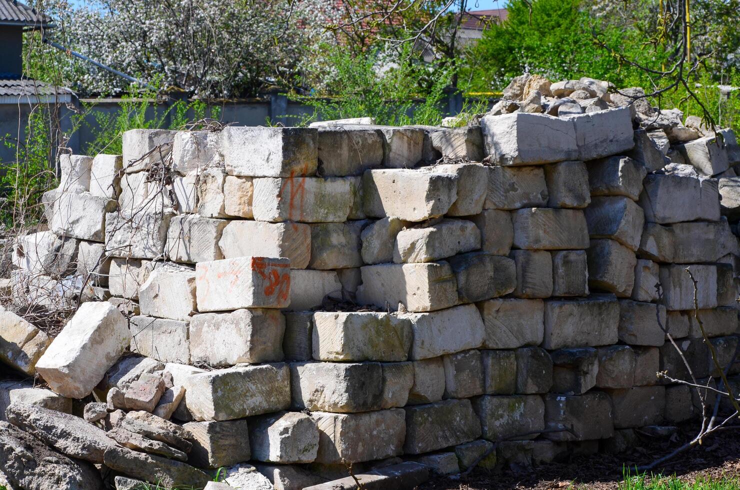 A pile of bricks is stacked in a corner of a yard. The bricks are old and worn, and the pile is quite large. The scene gives off a sense of abandonment and neglect photo