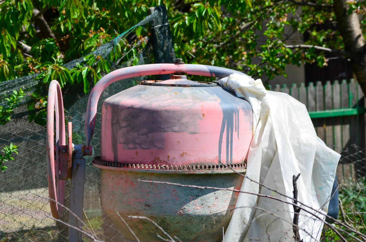 A rusty red cement mixer with a white plastic bag on top of it. The bag is torn and dirty photo