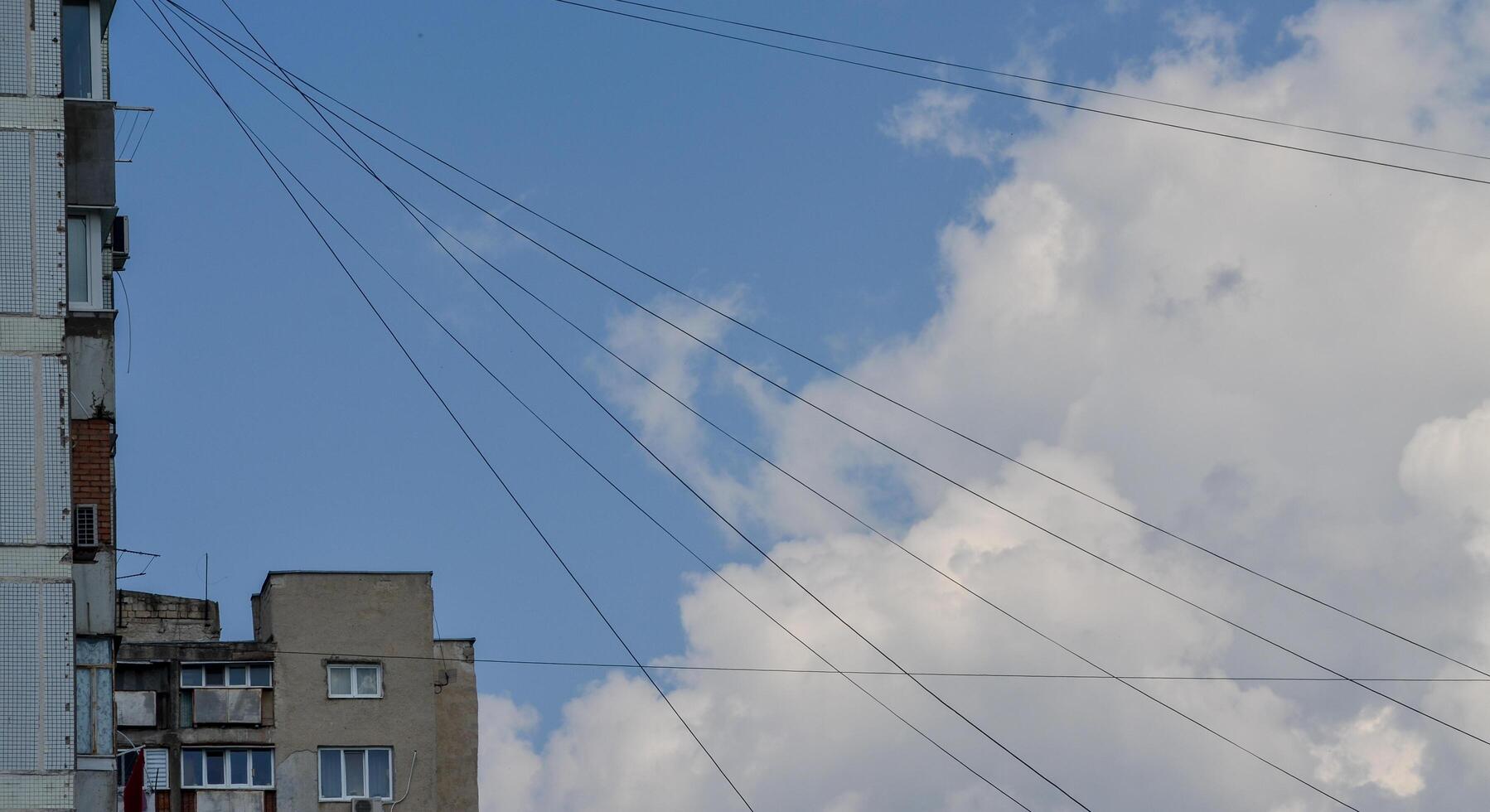 A building with a lot of wires above it. The sky is blue and there are clouds. The wires are connected to a power source photo