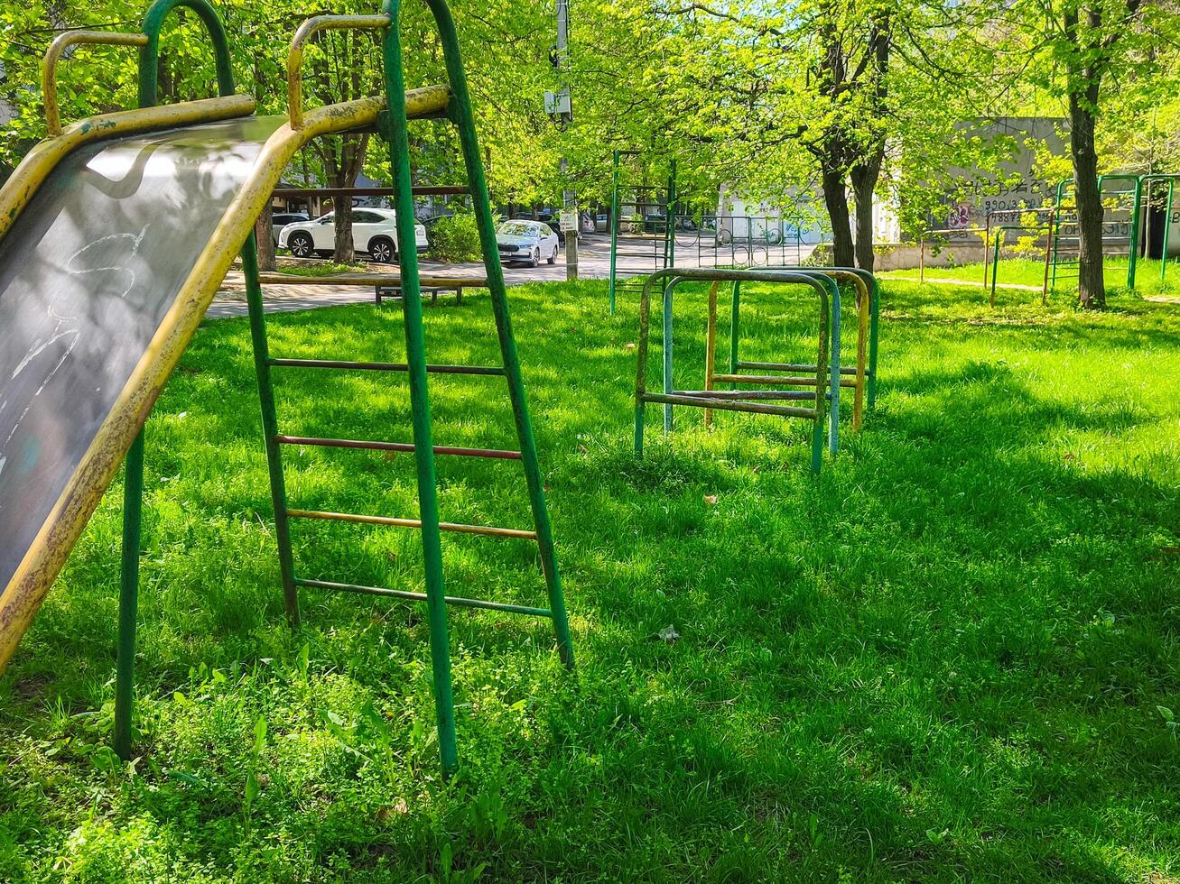 A park with a slide and a set of monkey bars. The slide is green and the monkey bars are silver. The park is empty and the grass is green photo