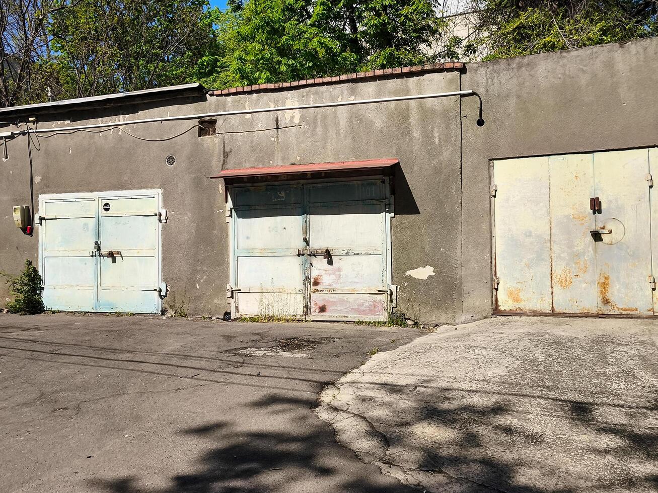 A row of old, rusted metal doors sit in front of a building. The doors are blue and white, and they appear to be locked. The scene is quiet and somewhat eerie photo