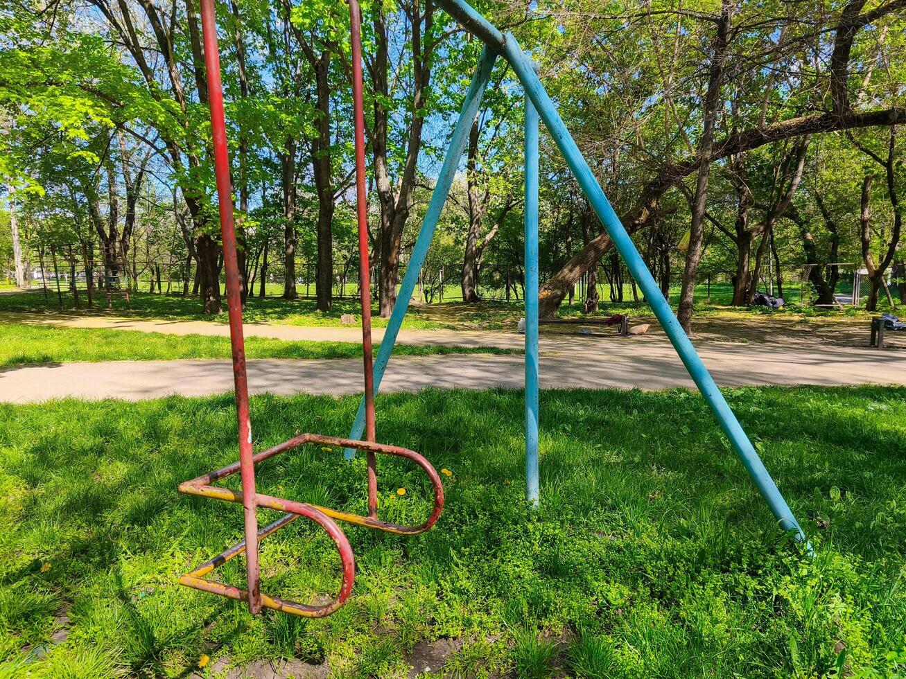 A rusty swing set is in a park with green grass. The swing set is old and rusted, and it is located in a grassy area photo