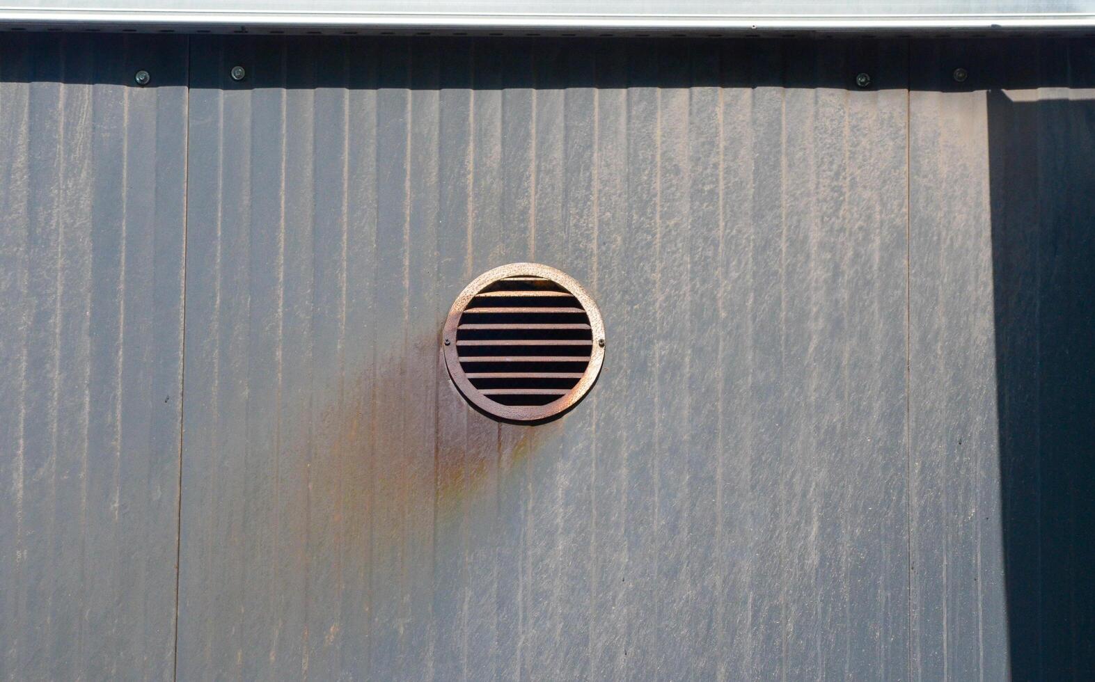 A vent is on the wall of a building. The vent is rusty and has a hole in it photo