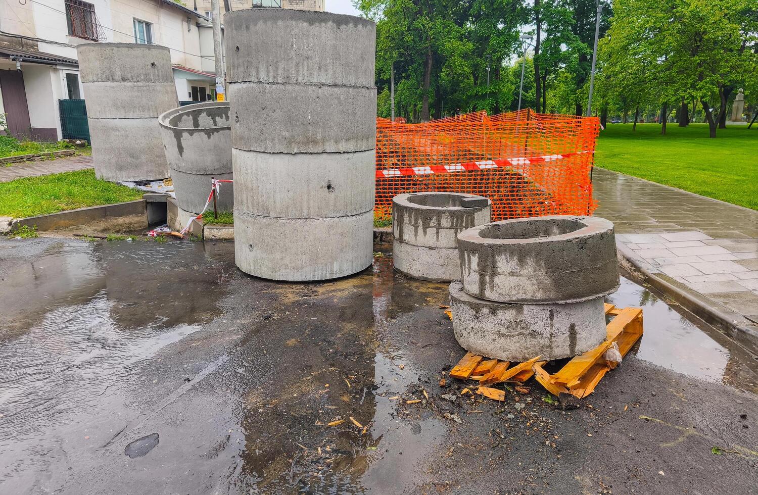 A construction site with a pile of cement blocks and a wooden pallet. The scene is wet and rainy, with a fence in the background photo