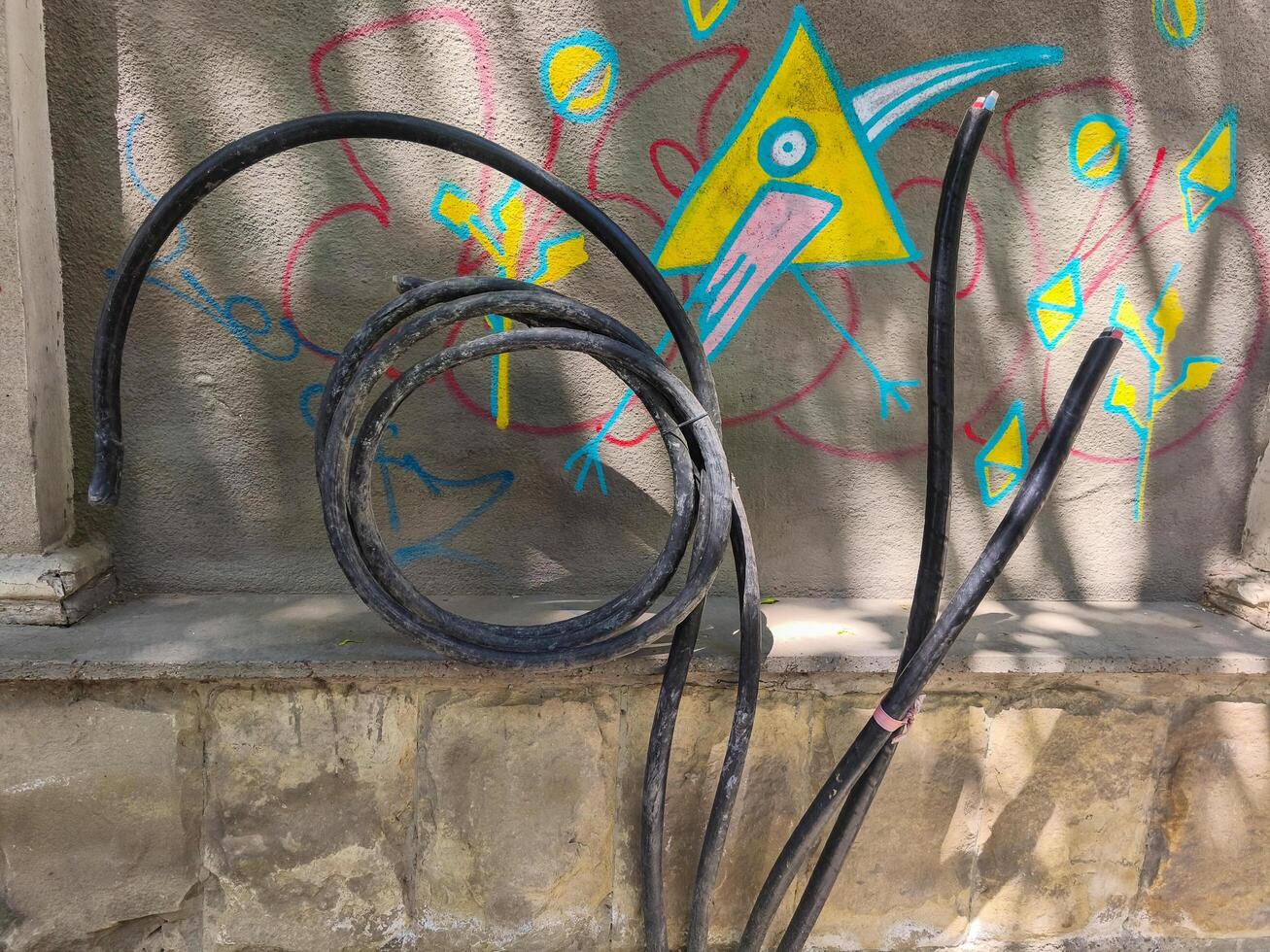 A black wire is hanging from a wall. The wire is twisted and bent. The wall is painted with bright colors photo