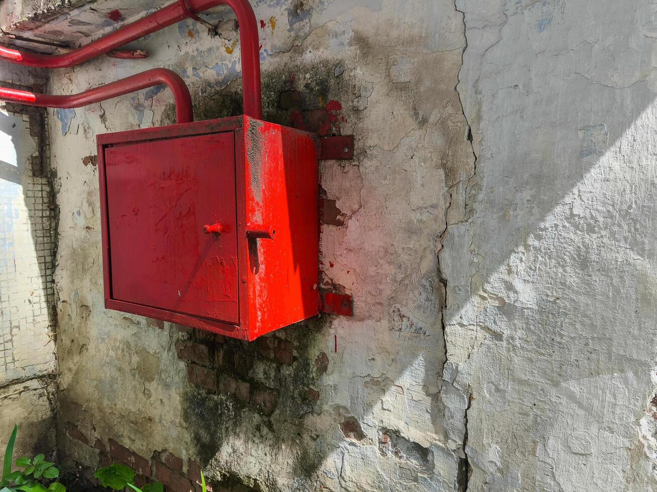 A red box with a red handle is sitting on a wall. The box is made of metal and has a red handle. It is located on a wall that is made of bricks and has a white paint photo