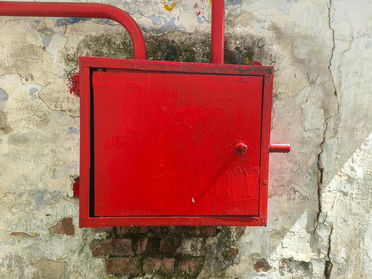 A red metal box with a handle sits on a wall. The box is made of metal and has a red color photo