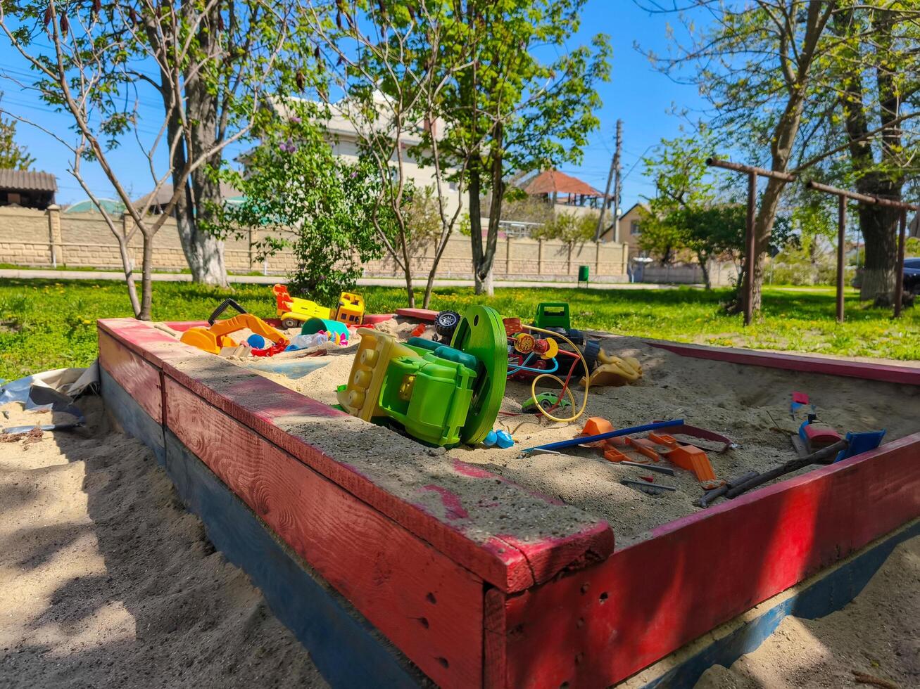 A red and blue sandbox with toys in it. The sandbox is empty and the toys are scattered around it photo