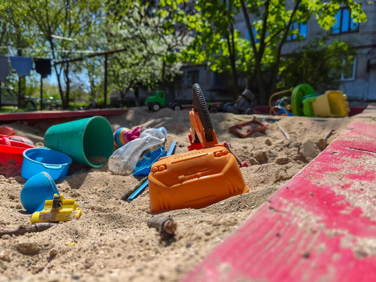 A pile of toys and a toy car are on the sand. The toys are scattered and the car is in the middle of the pile. The scene is messy and disorganized photo