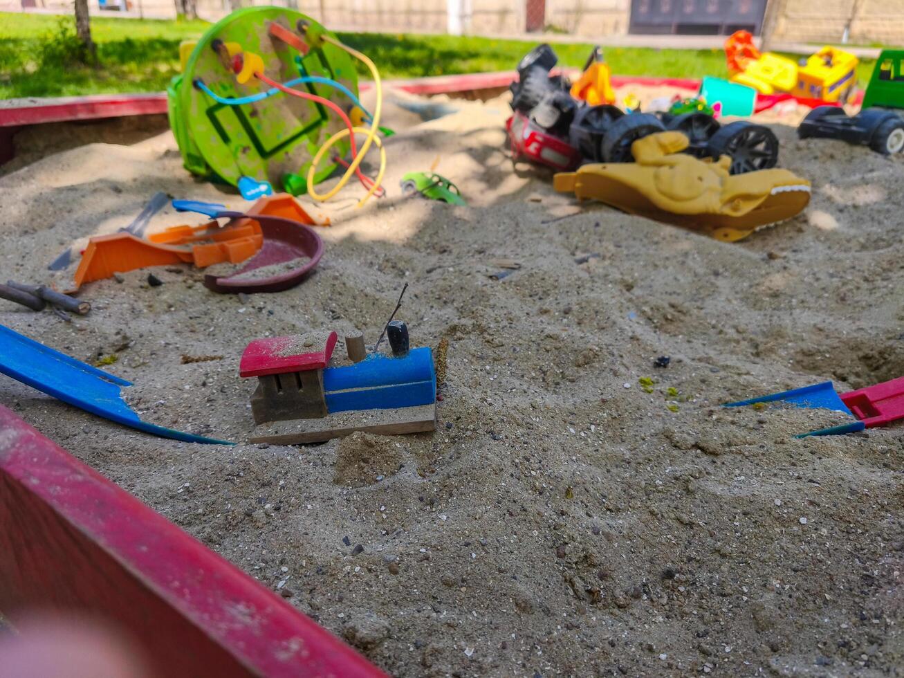 A pile of toys, including a train, are scattered in a sandy area. The scene is playful and fun, with the toys scattered around in various positions photo