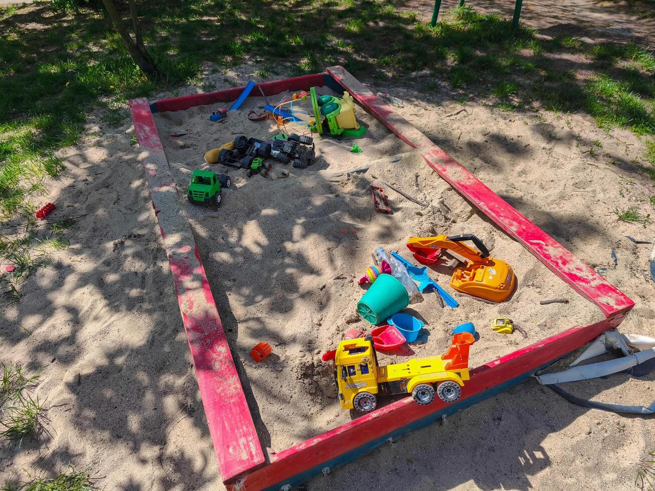 A red sandbox with toys in it. The toys include a truck, a car, and a shovel photo