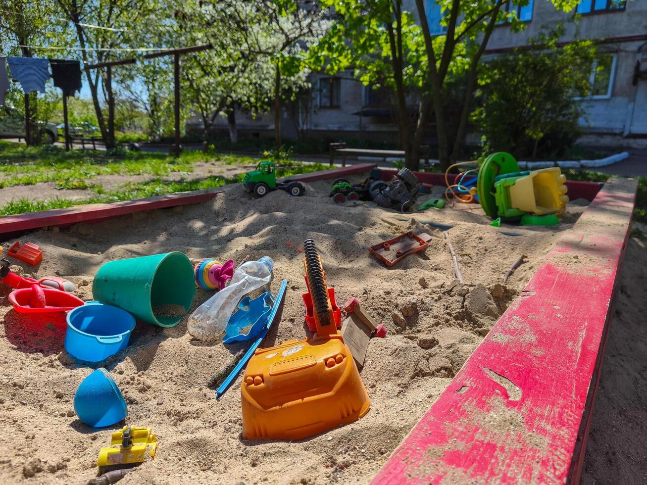 A pile of toys and plastic cups are scattered on the sand in a park. The scene is messy and disorganized, with no clear purpose or direction. Scene is chaotic and unkempt photo