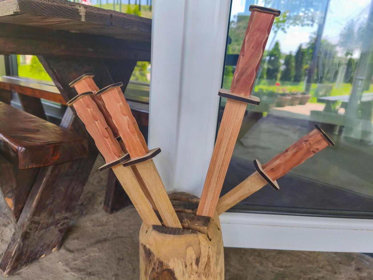 A wooden vase with four wooden sticks in it. The sticks are arranged in a way that they look like swords. The vase is placed on a table outside photo
