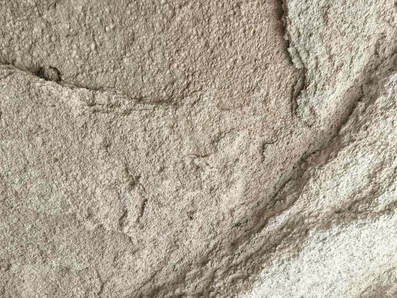 A wall with a rough texture and a few cracks. The wall is made of cement and has a grey color photo
