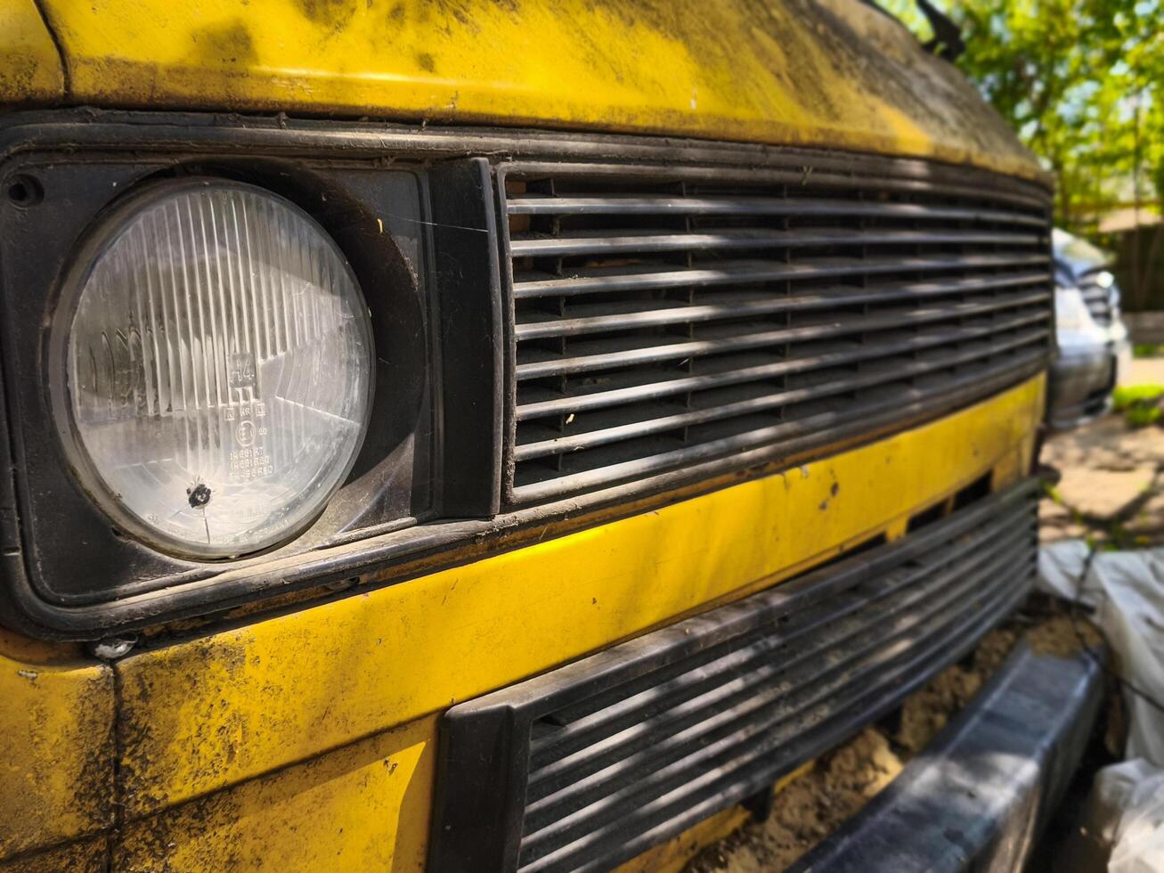 A yellow van with a dirty grill and a black headlight. The headlight is missing a bulb photo