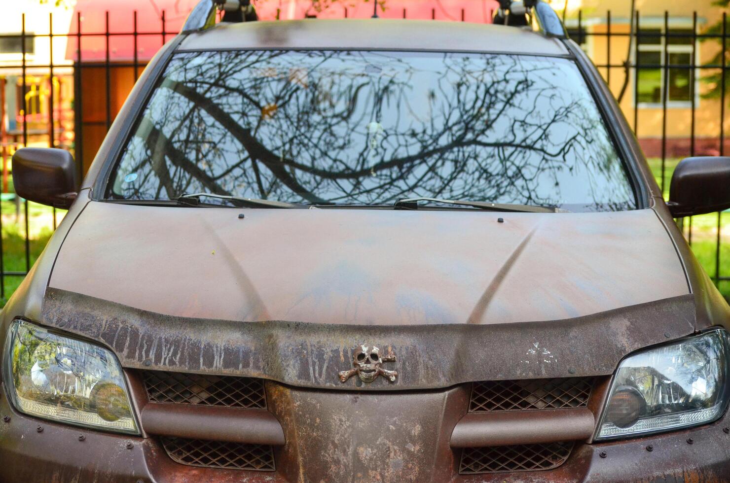 A car with a skull on the hood and a skull on the grill. The car is dirty and has a rusty appearance photo