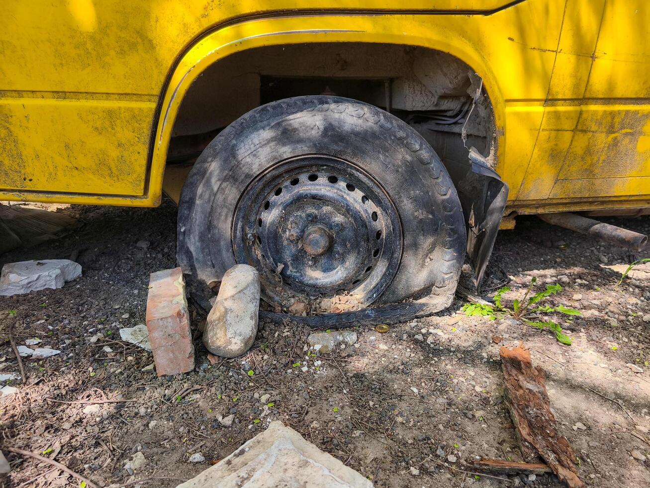 A yellow bus with a black tire on the ground. The tire is missing and there is a brick on the ground next to it photo