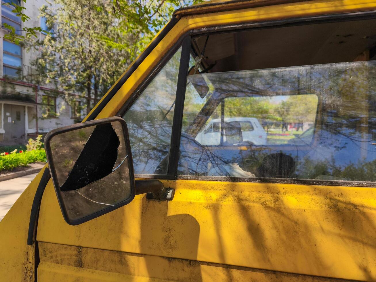 A yellow car with a broken mirror. The mirror is black and the car is parked in front of a building photo