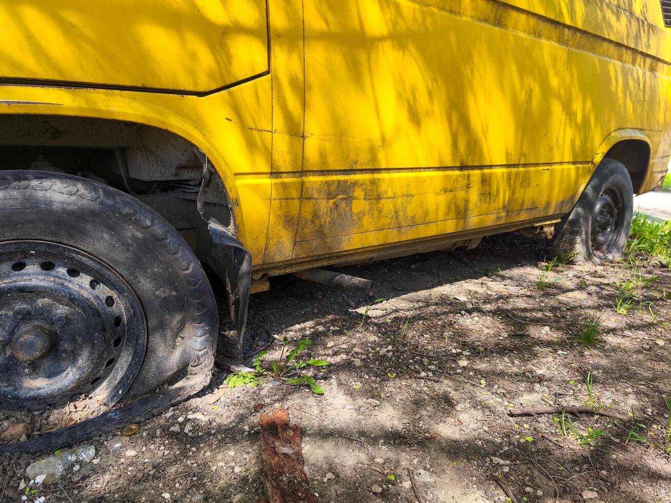 A yellow van with a flat tire is parked on the side of the road. The tire is missing and the van is covered in dirt photo