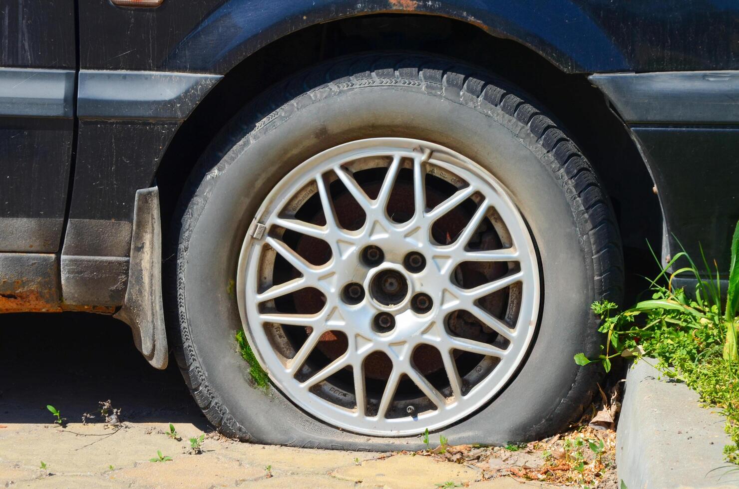 A black car with a flat tire. The tire is missing a piece and is sitting on the ground photo