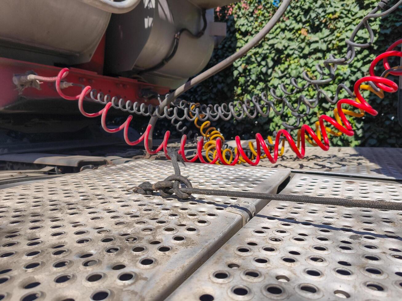 A red and yellow tire is attached to a chain. The chain is wrapped around the tire and is connected to a red and yellow hose. The tire is on a metal surface photo