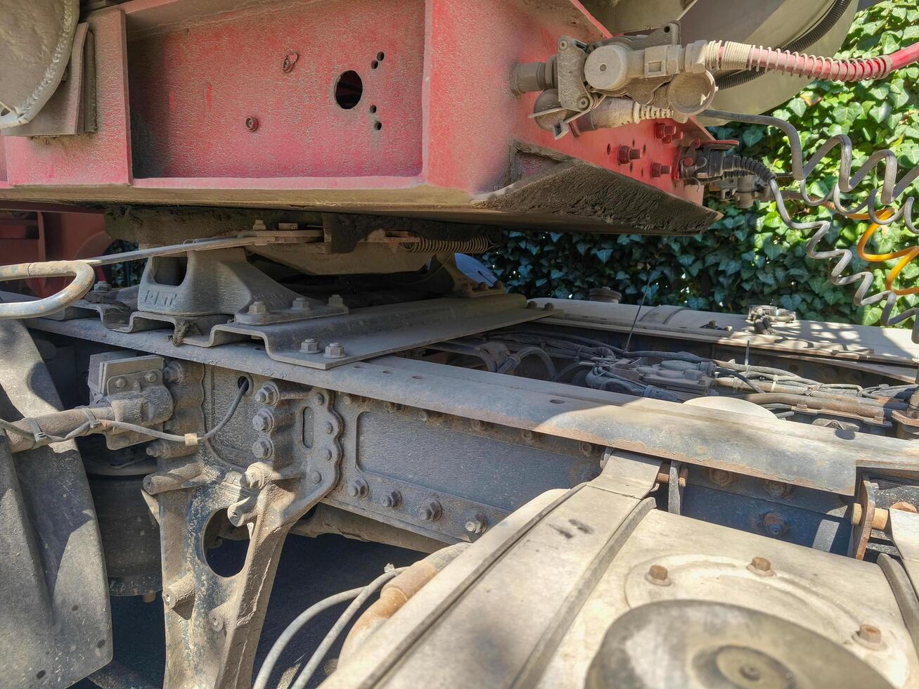 A dirty truck with a red frame. The truck is parked in a grassy area. The dirt on the truck is visible and it is old photo