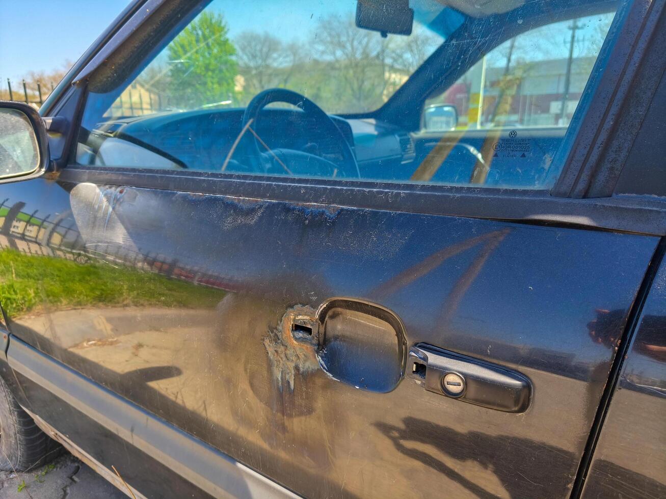 A car door is open and the door handle is missing. The door is dirty and the car is parked in a parking lot photo
