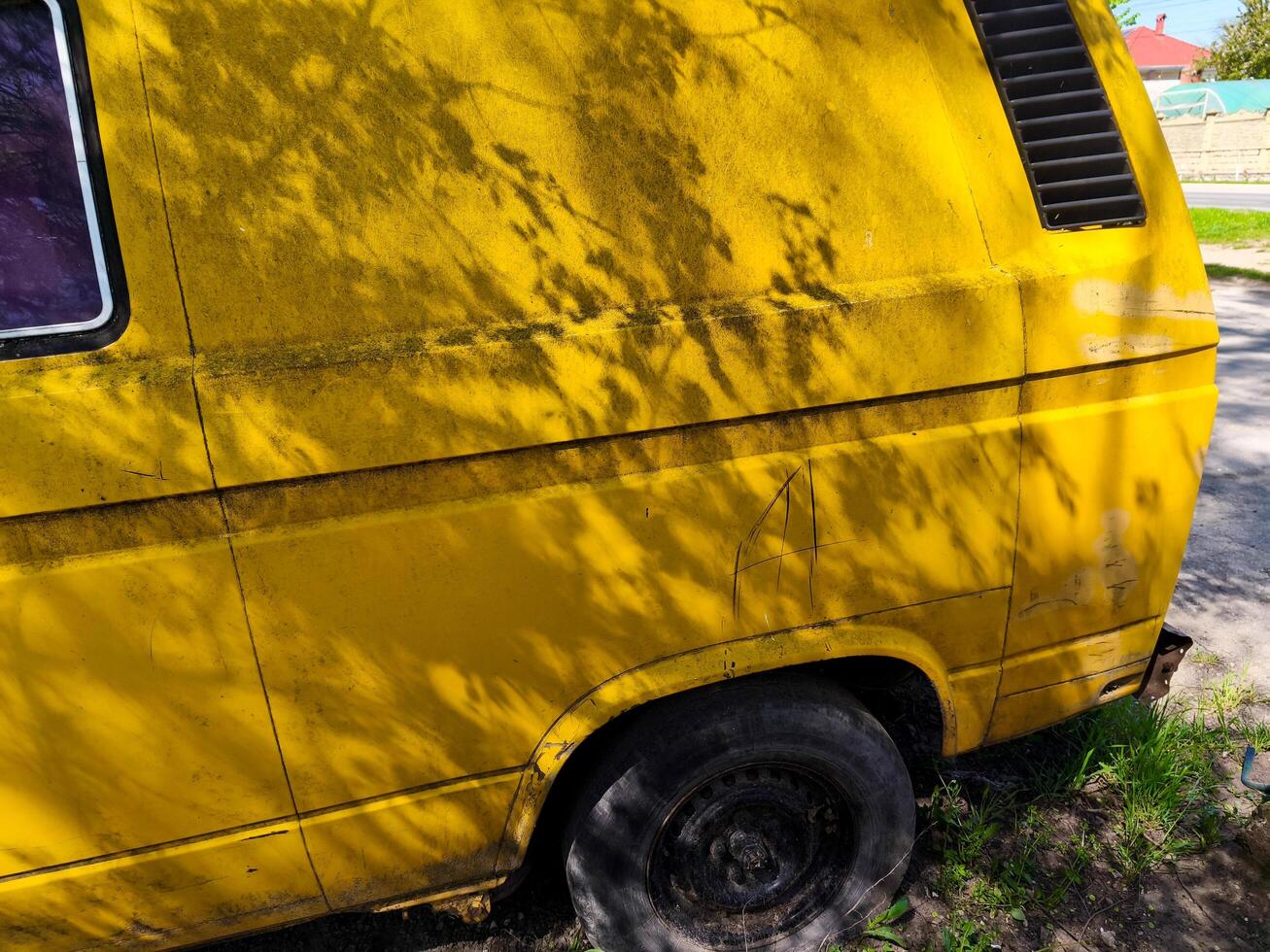 A yellow van with a dirty back and a black tire. The van is parked on the side of the road photo