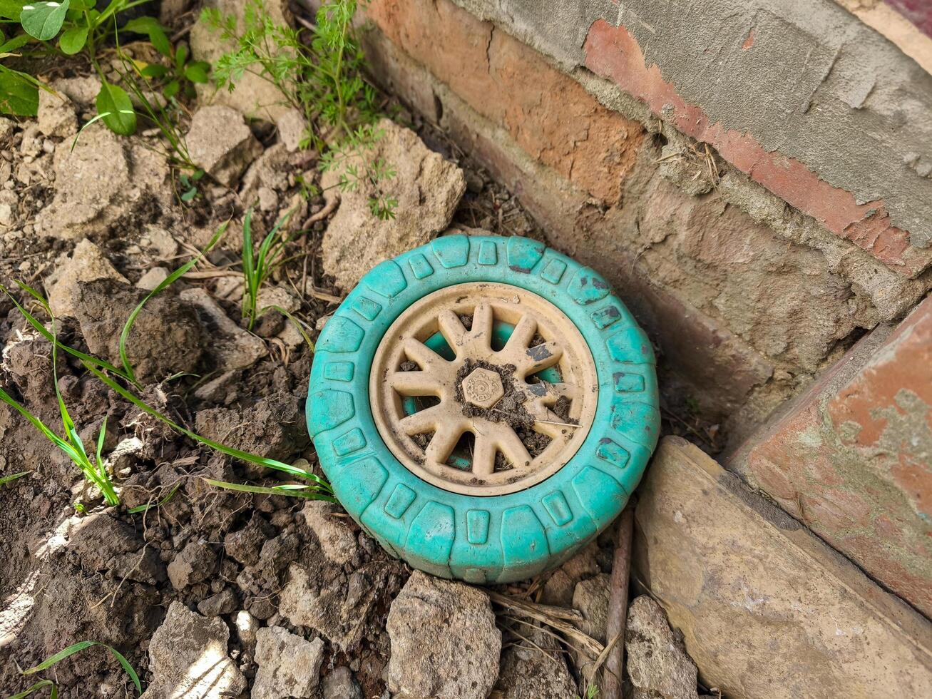 A green wheel is laying on the ground next to a brick wall. The wheel appears to be old and dirty, and it is surrounded by dirt and rocks. The scene gives off a sense of abandonment and neglect photo