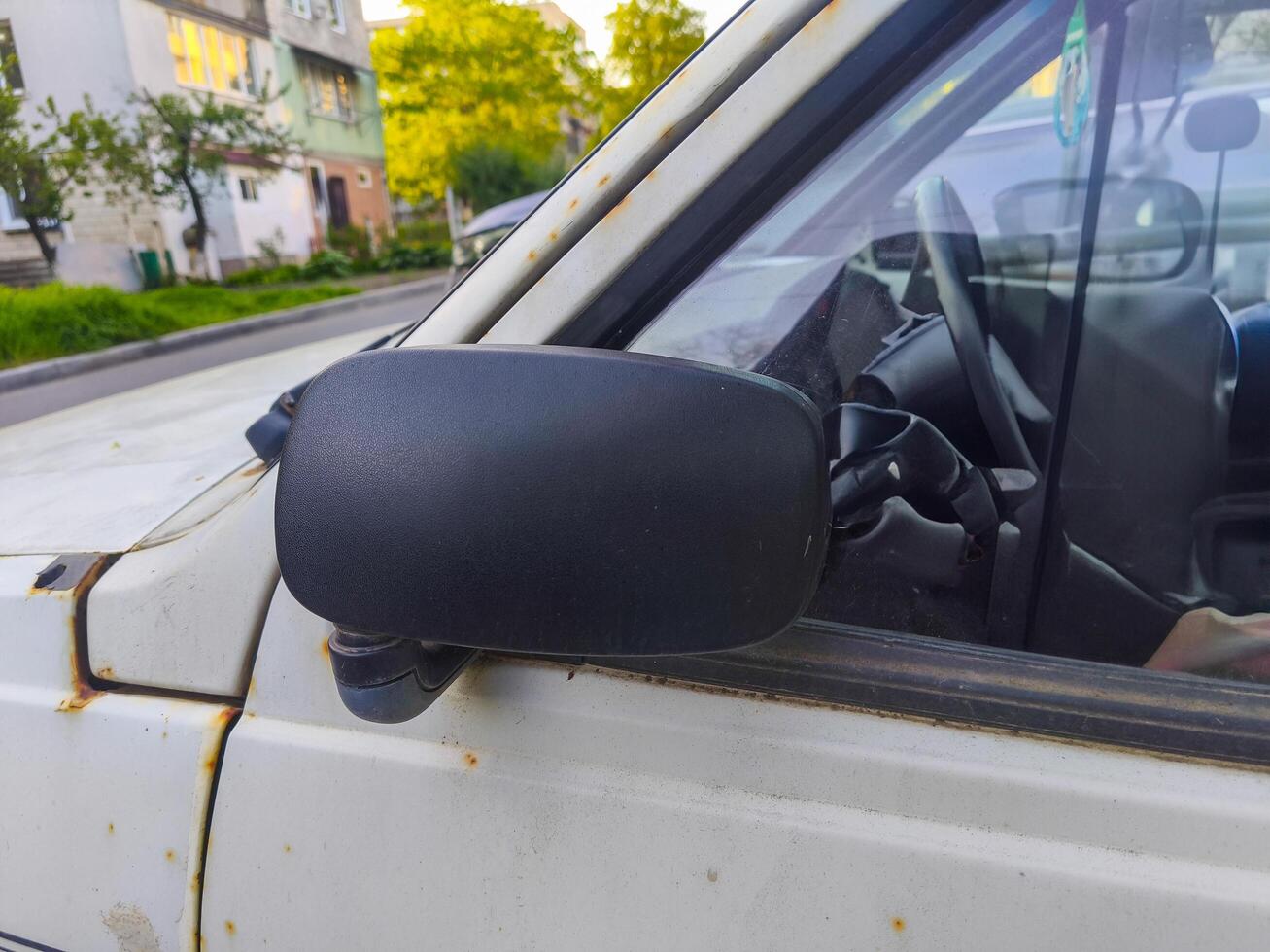 A dirty car mirror is on the side of a road. The mirror is black and has a rusted appearance photo