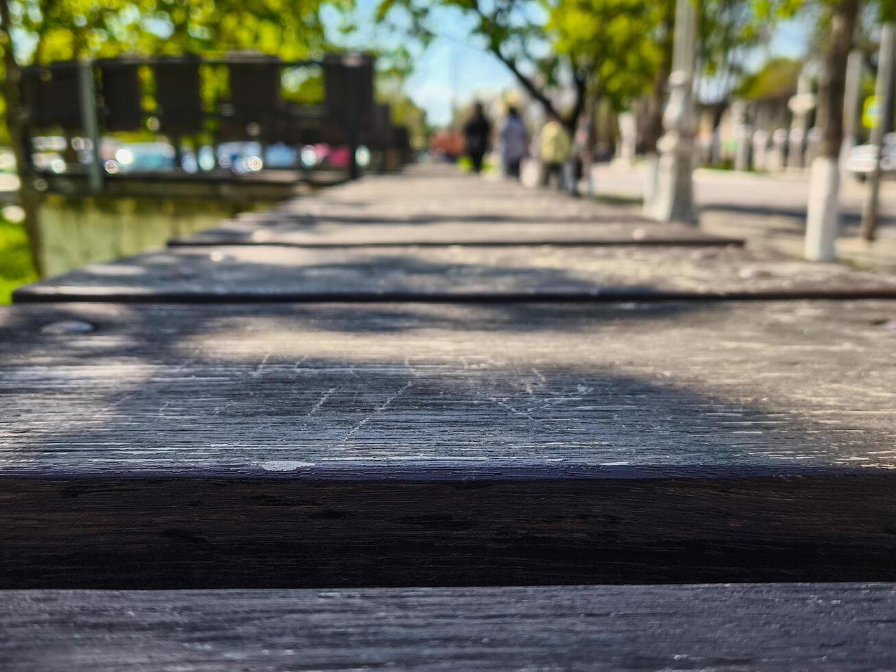 A wooden bench with a view of a city street. The bench is empty. The street is busy with cars and pedestrians photo